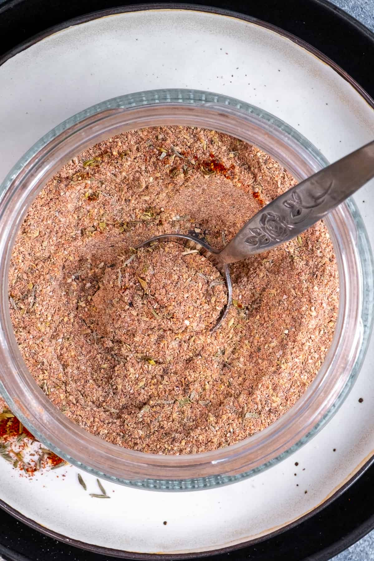Chicken seasoning spices in a glass jar and a spoon in it.