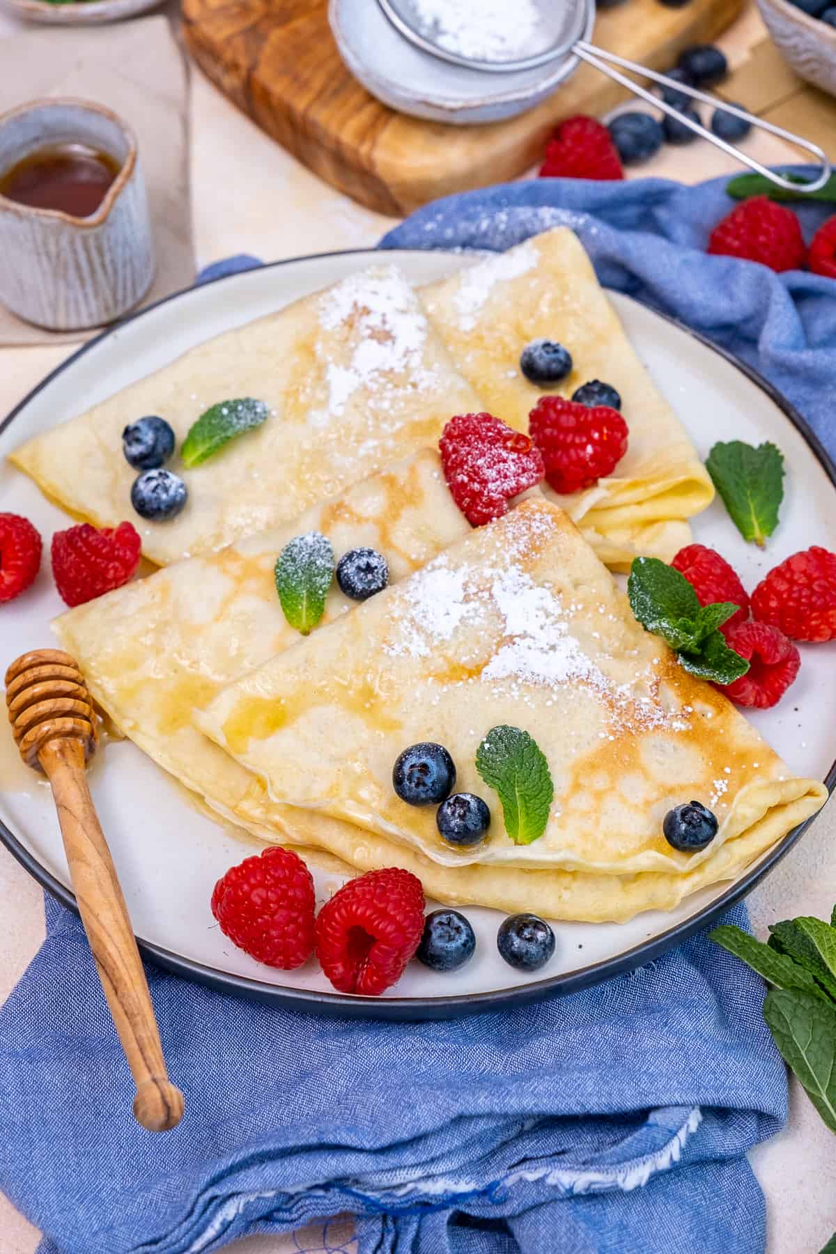 Crepes with powdered sugar, fresh berries and mint leaves on a plate.