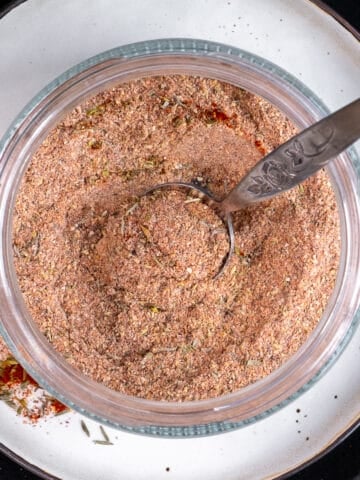 Chicken seasoning in a glass jar and a small spoon in it.