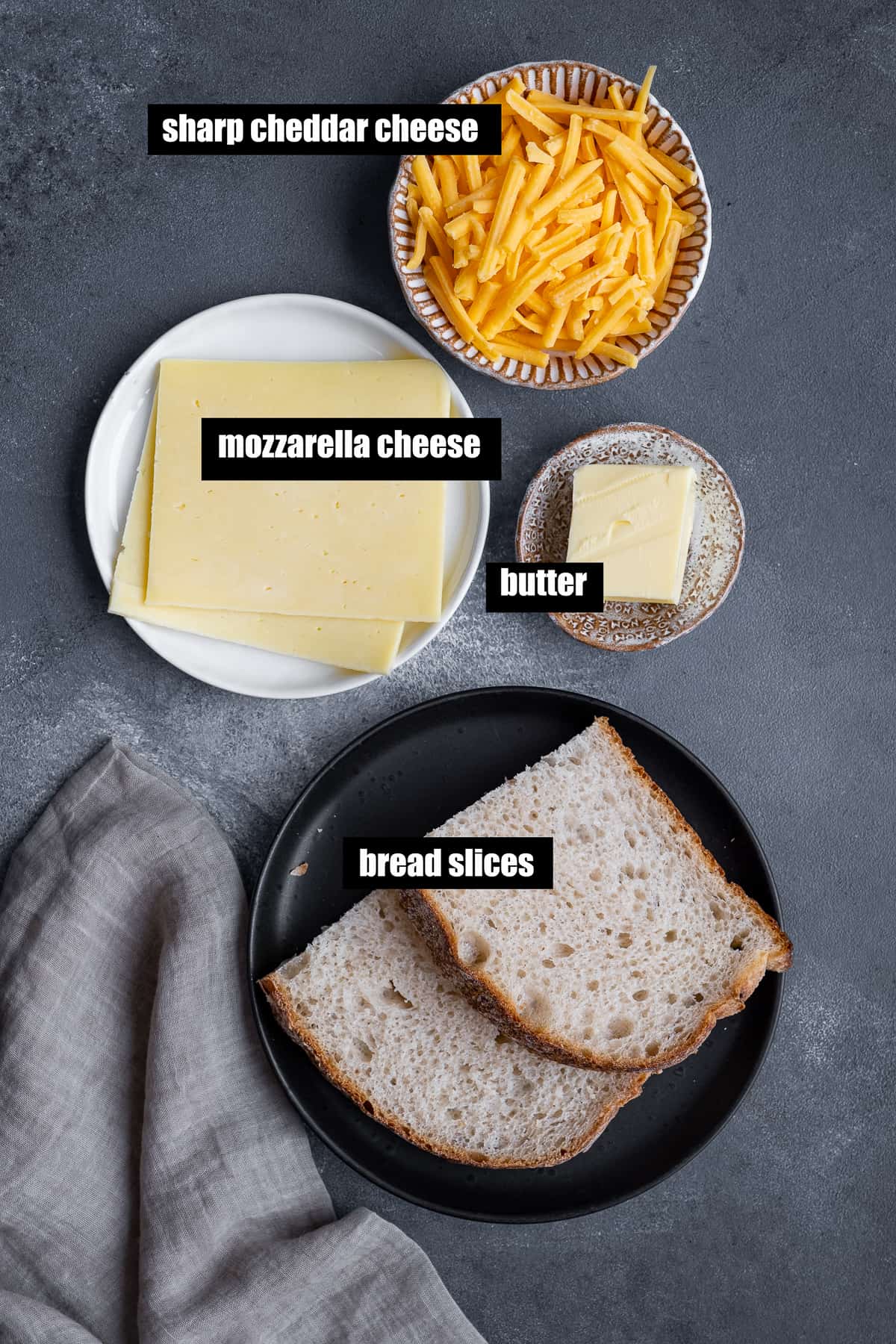 Cheese slices, shredded cheese, butter and bread slices on a dark background.