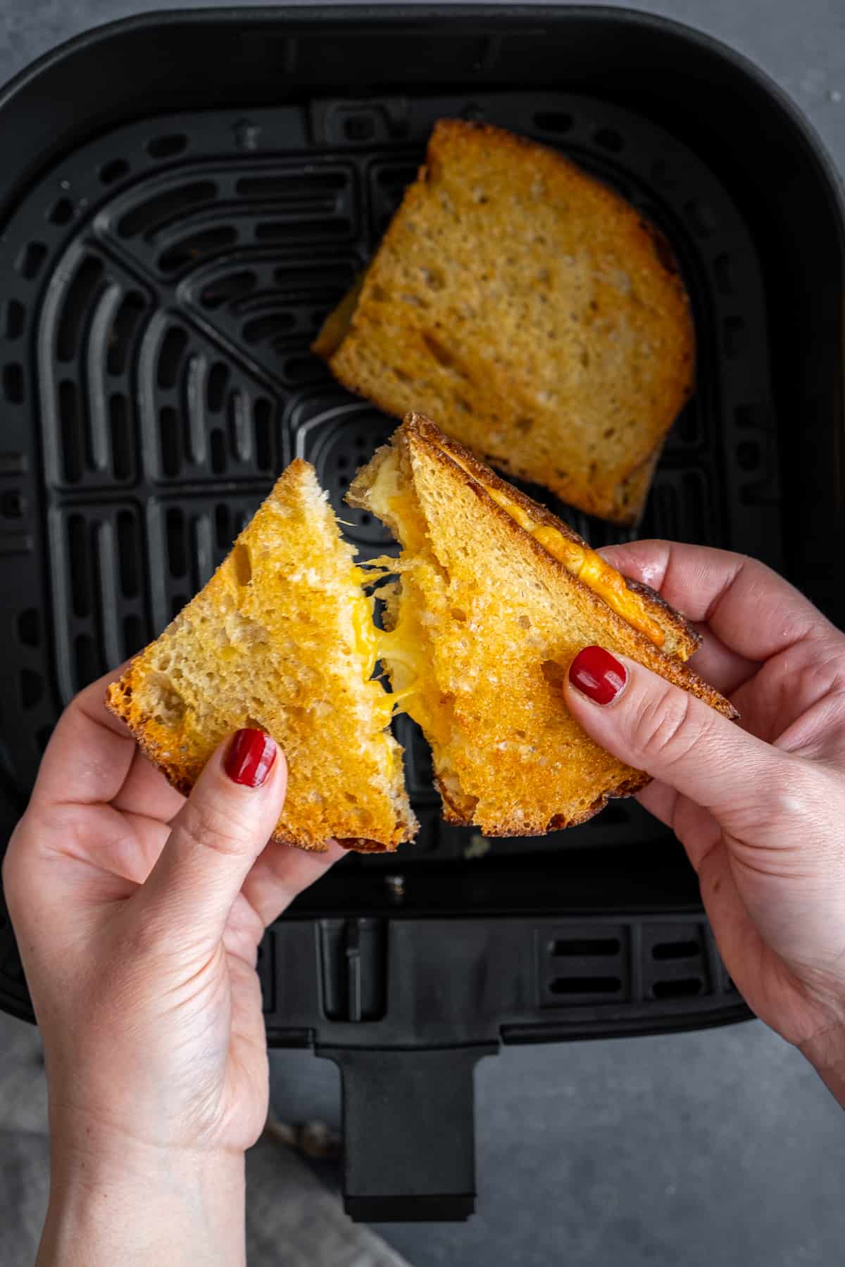 Hands pulling a grilled cheese sandwich apart and melting cheese in the center being shown.