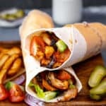 Chicken doner wraps on a wooden board, pickled, French fries, tomato and onion slices on the side.