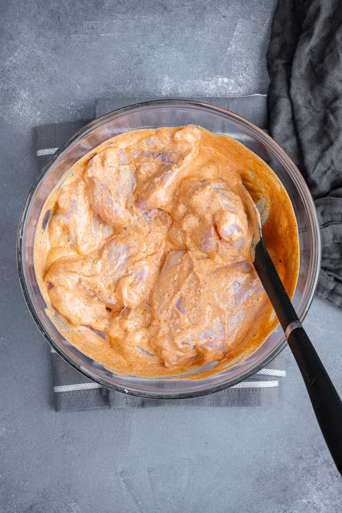 Chicken thighs in yogurt marinade in a glass mixing bowl.