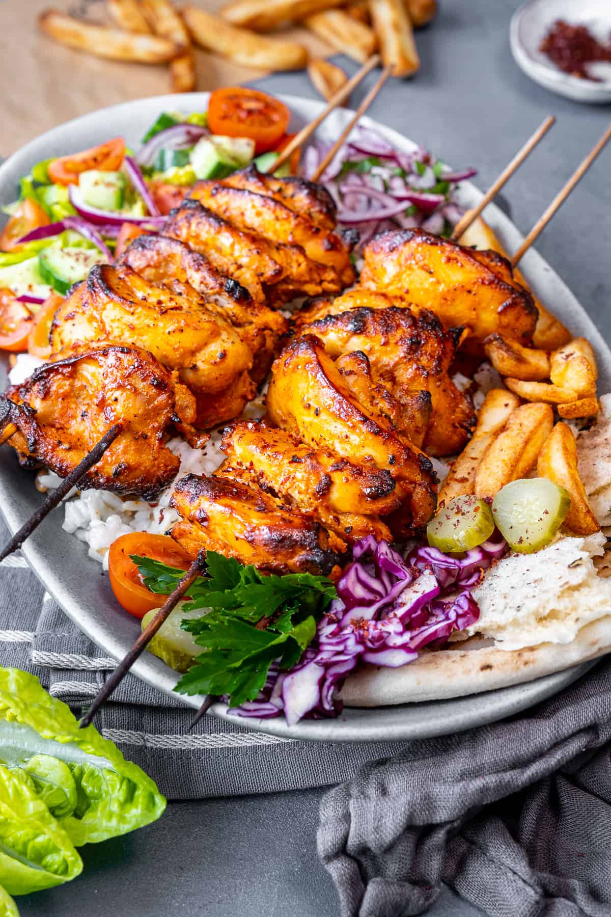 Chicken doner kebab skewers on rice and salad, pickles and French fries accompany on the same oval plate.