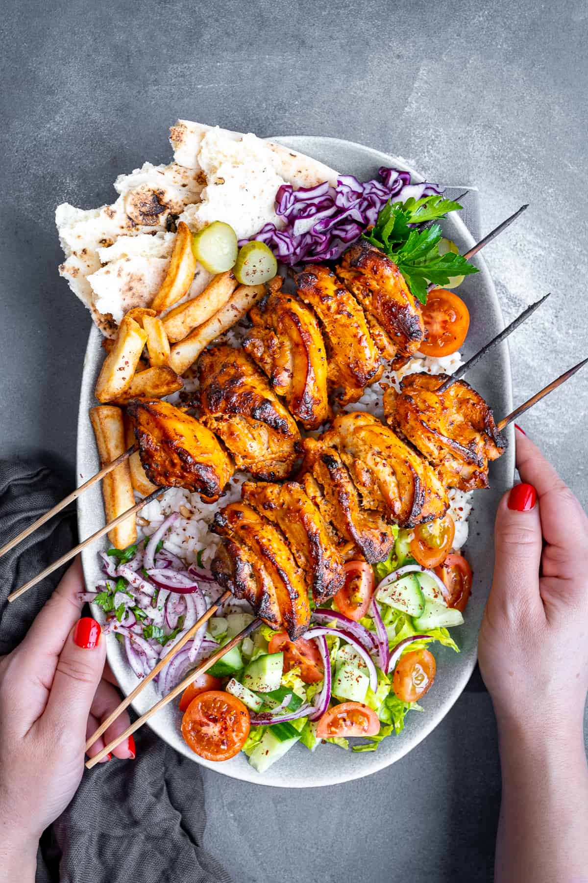 Hands holding a plate loaded with rice, salad, chips, pickles and chicken doner kebab.