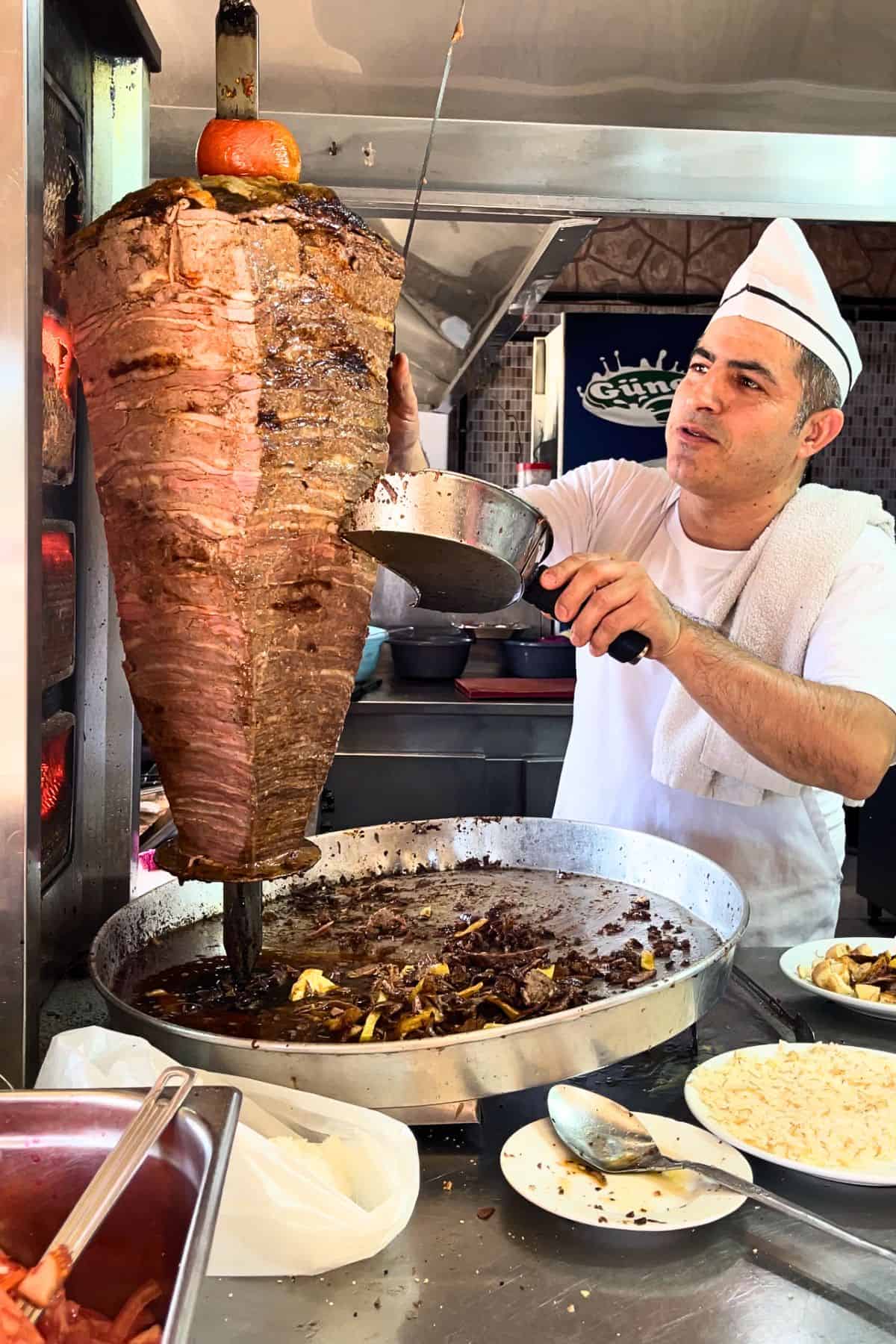 Chef slicing beef doner kebab from a vertical rotisserie, with layers of meat and fat visible, in a Turkish doner shop.