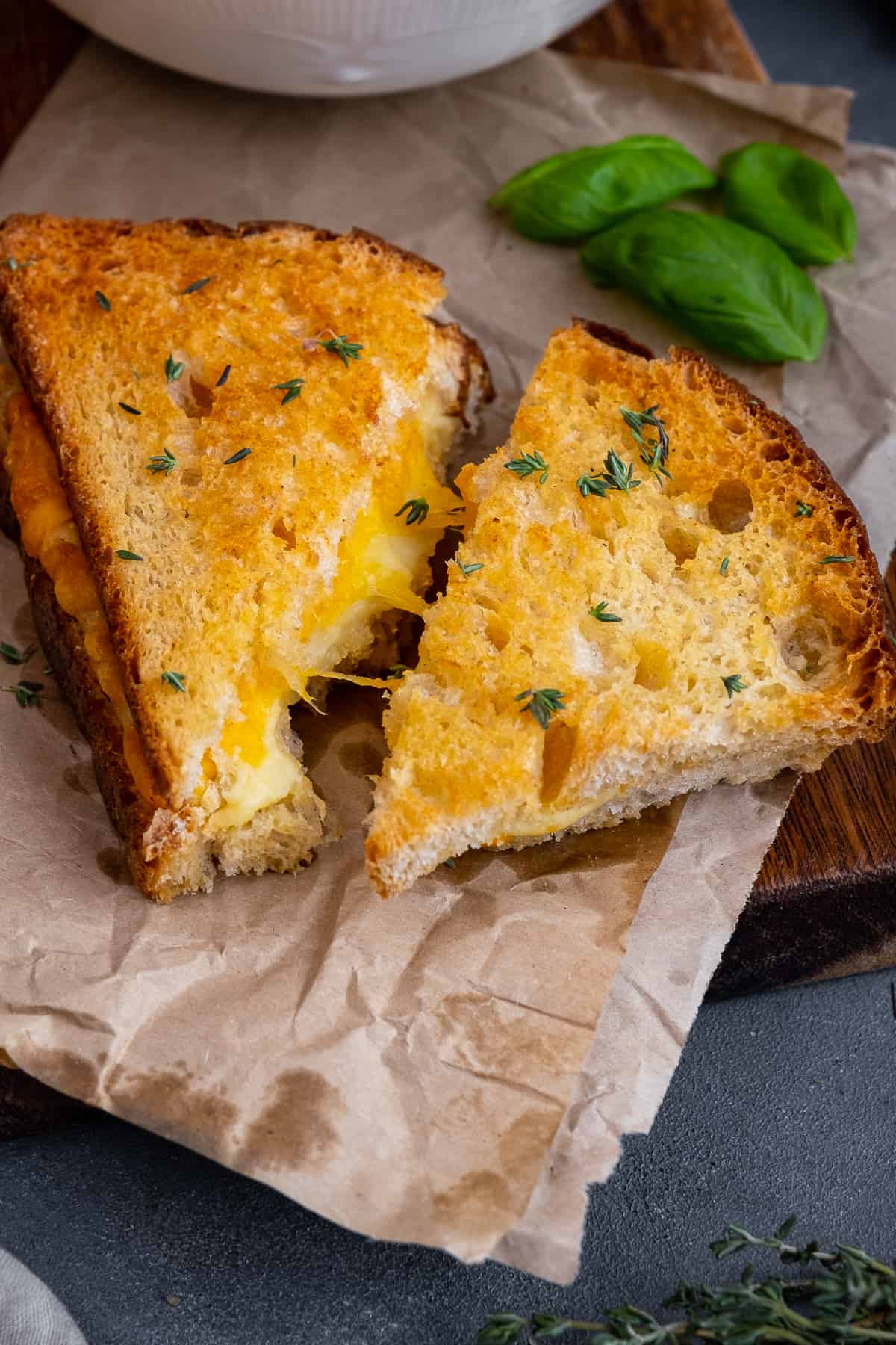 Grilled cheese sandwiches garnished with thyme and basil leaves behind them.