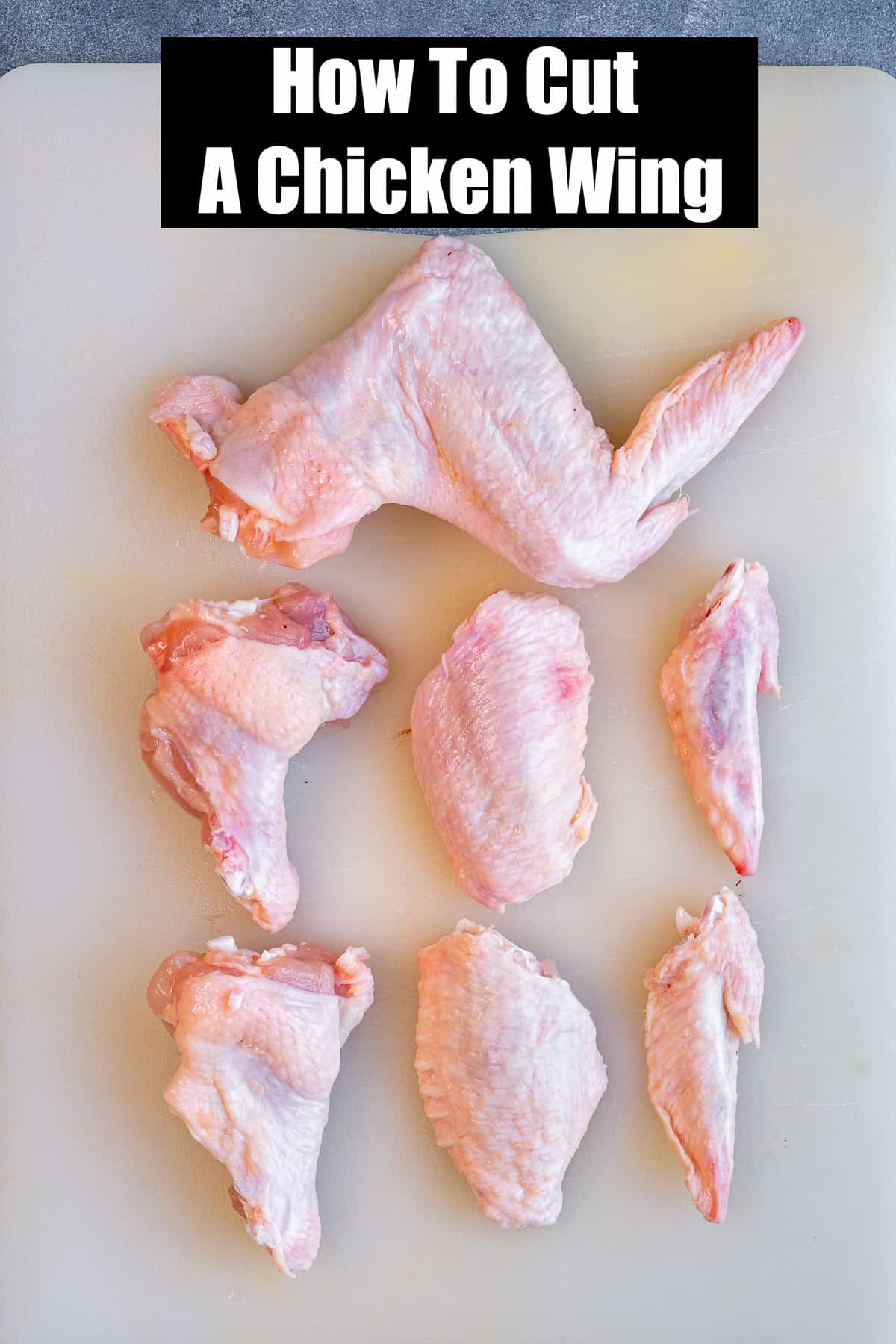 A whole chicken wing, drumettes, flats and wing tips on a white cutting board.