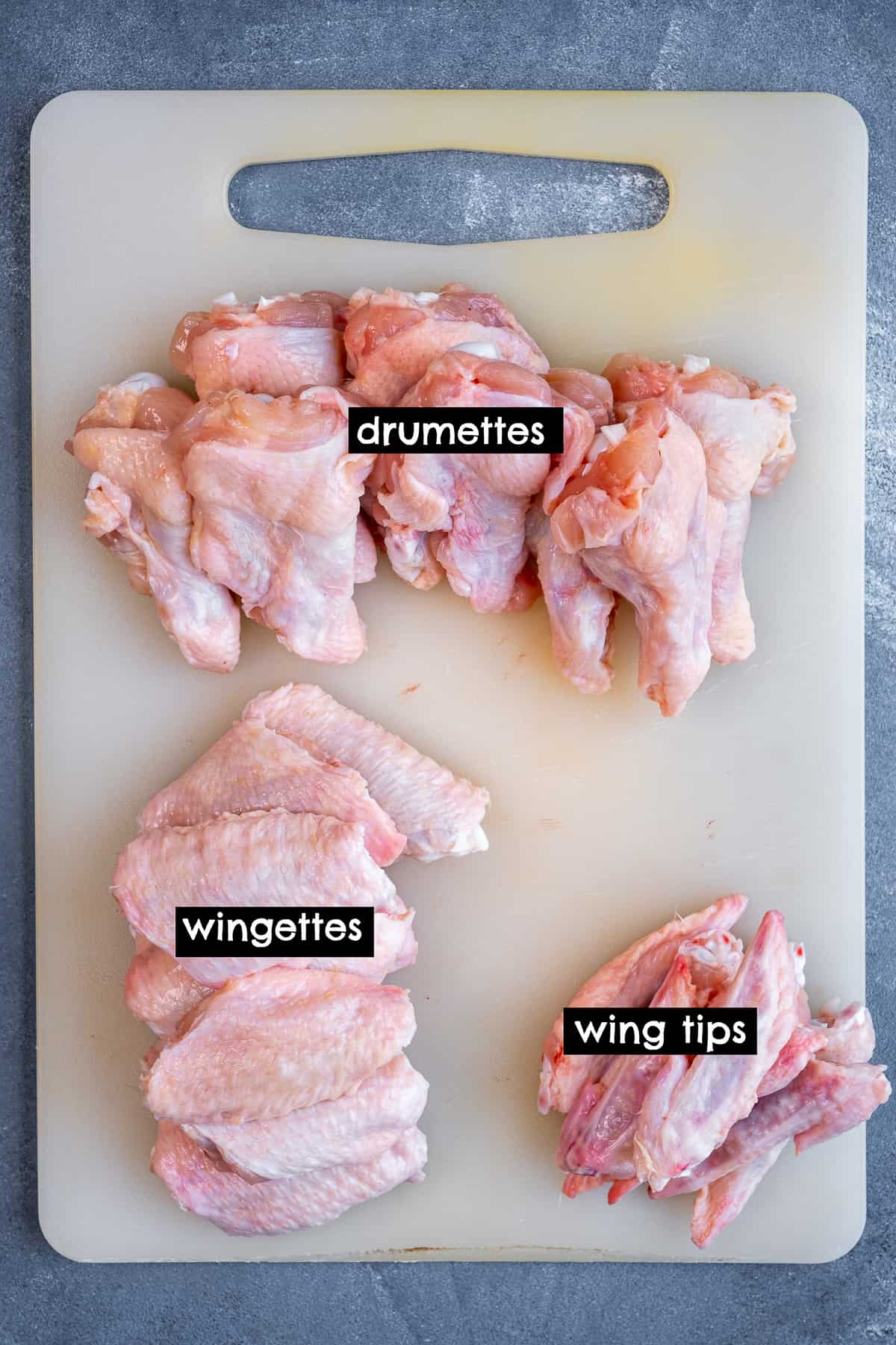 Chicken drumettes, wingettes and wing tips piled in groups on a cutting board.