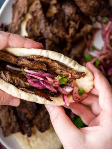 Hands holding doner sandwich with onions.