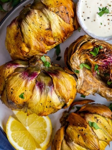 Close shot of air fried artichokes served with lemon slices and a dipping sauce on the side.