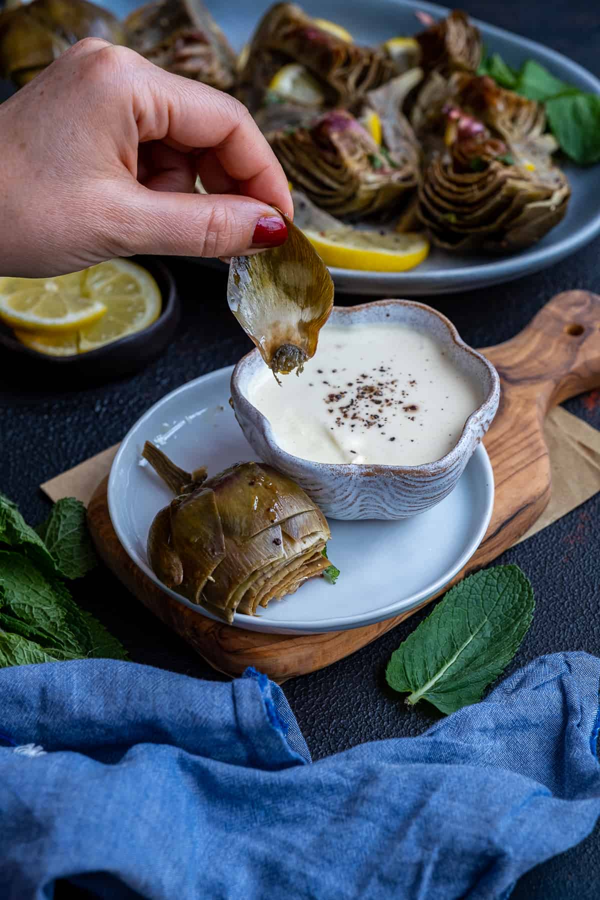 Woman hand about to dip a leaf of a steamed artichoke into a yogurt and mayonnaise dipping sauce.