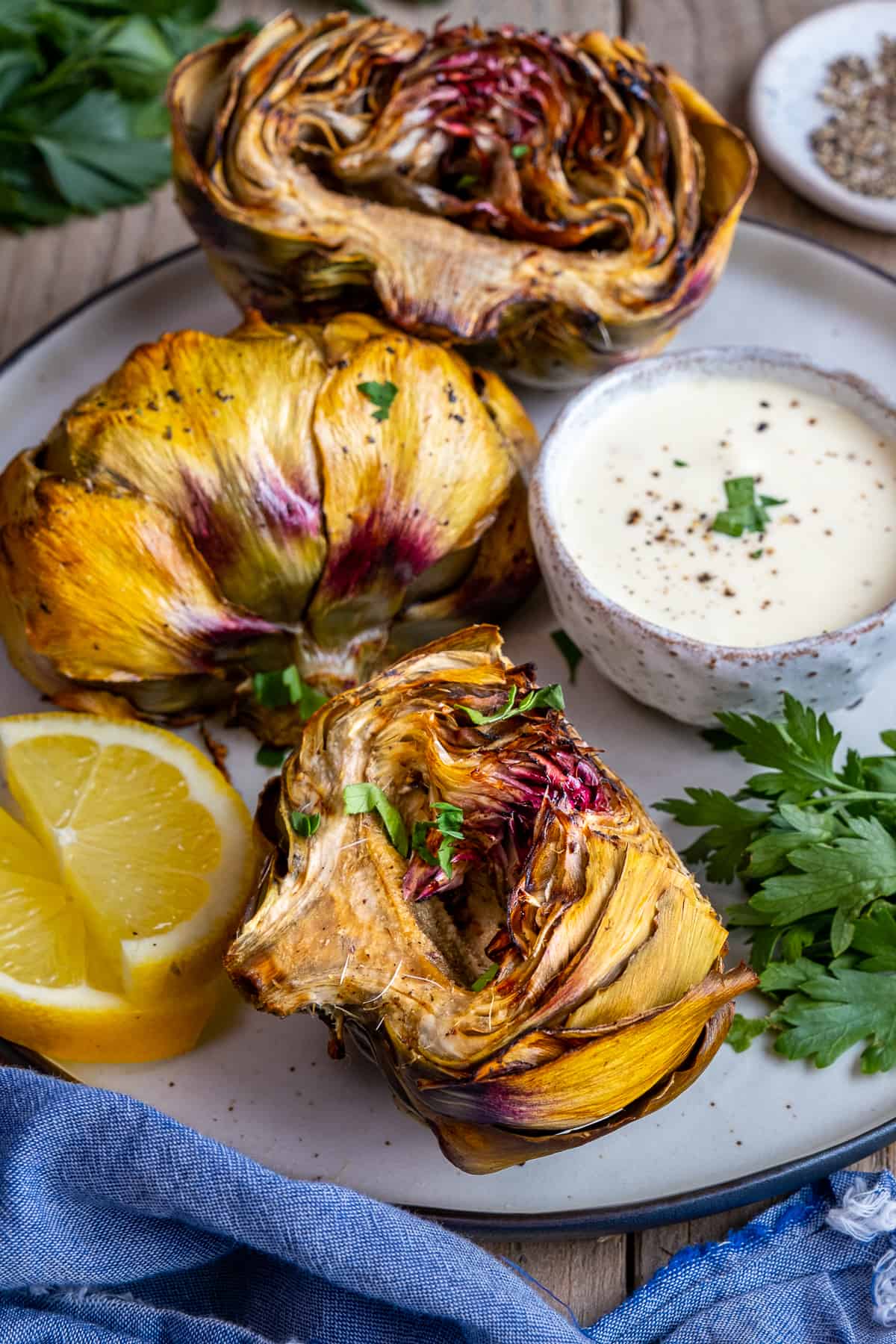 A close shot of air fried artichokes served with lemon slices and a dipping sauce.