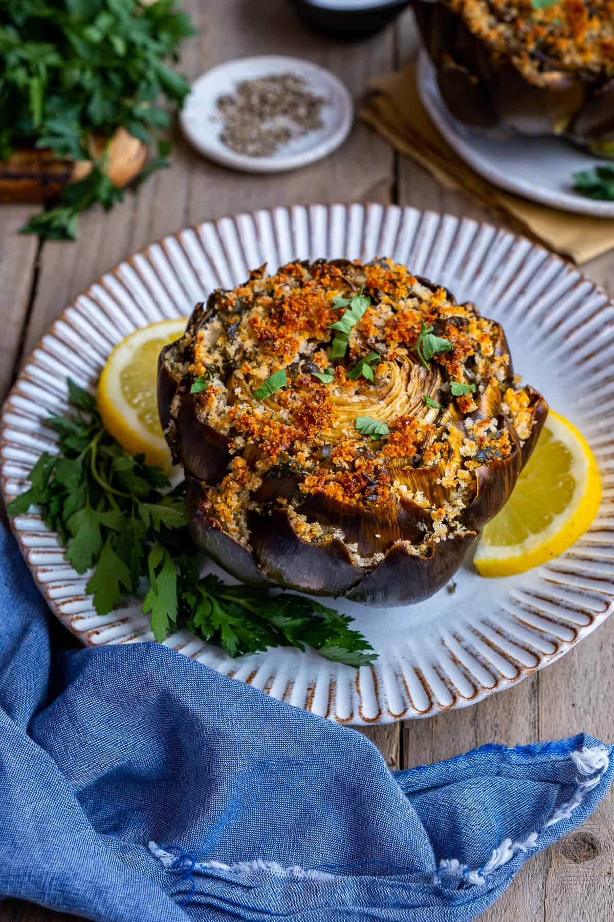 Stuffed artichoke on a white plate garnished with parsley and lemon slices.