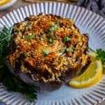 A stuffed artichoke served on a white plate garnished with chopped parsley and a lemon slice.