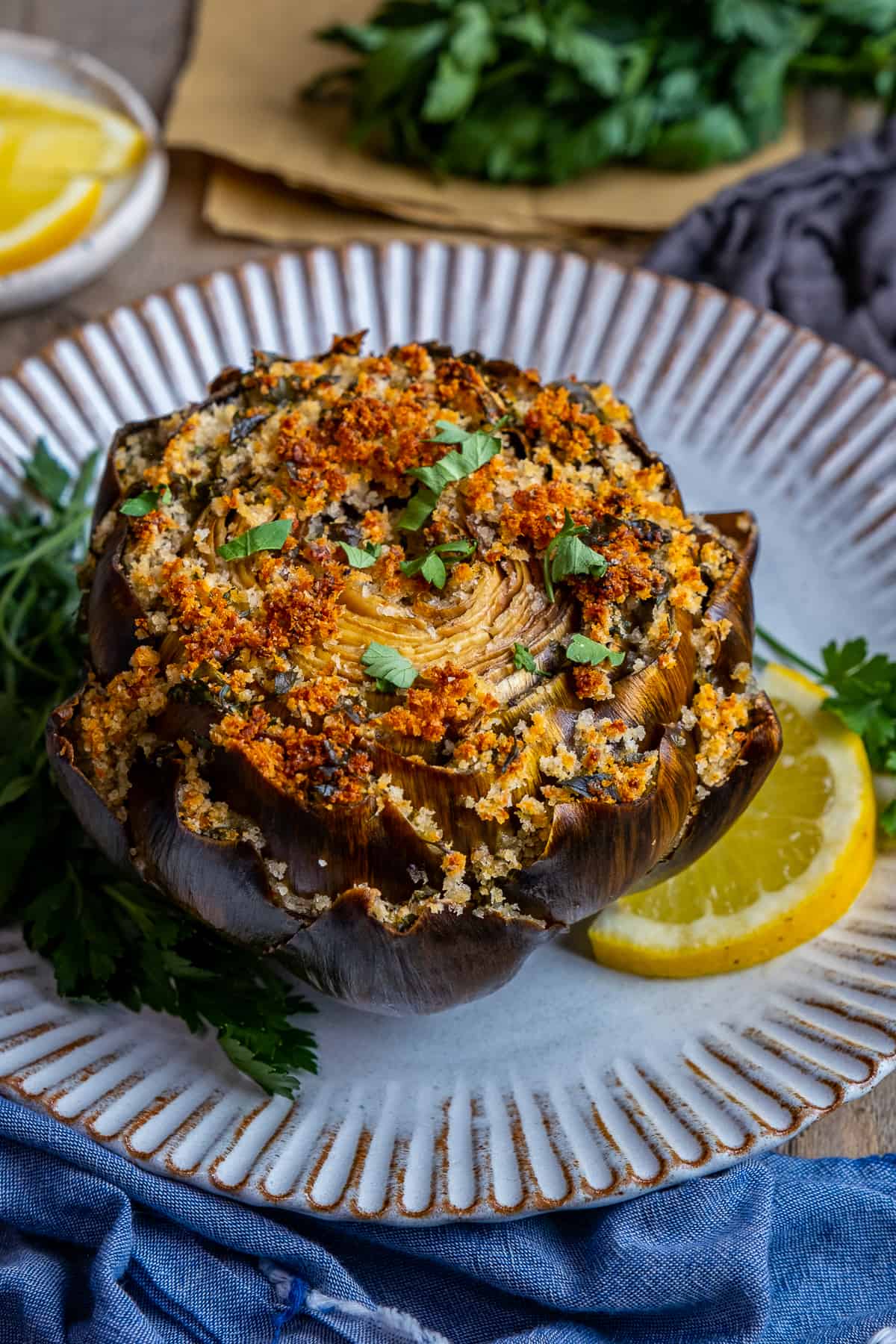 A stuffed artichoke garnished with parsley and a lemon slice on a white plate.