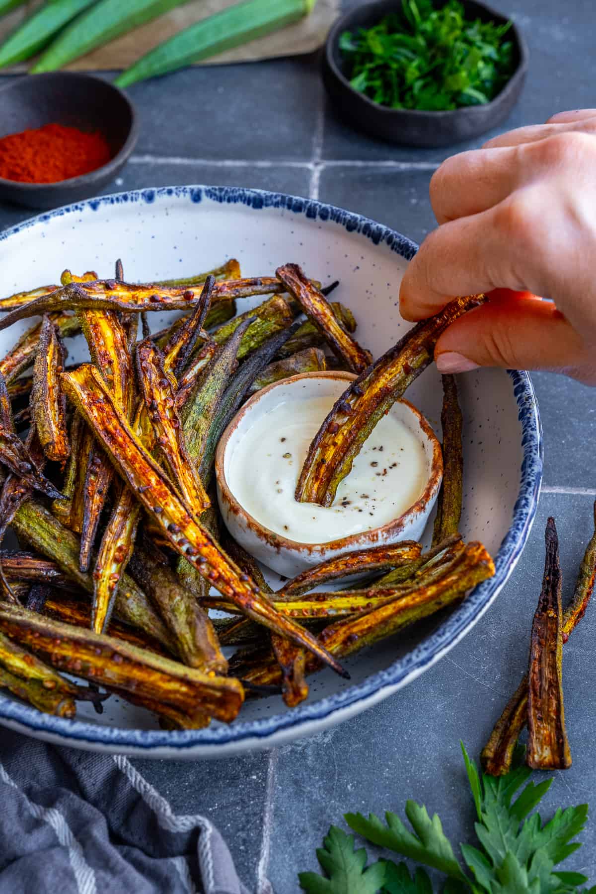 A hand dipping a piece of fried okra into a yogurt sauce.