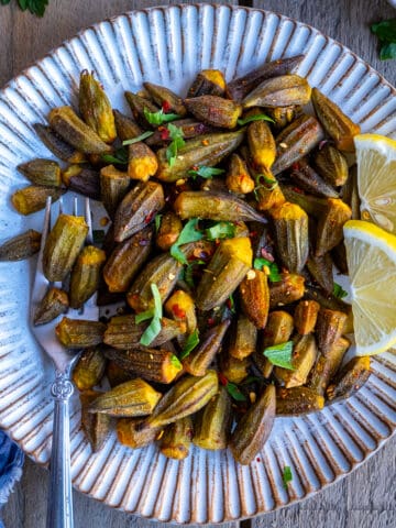 Fried okra garnished with parsley and lemon slices on a white plate.