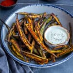 Crispy okra fries in a white bowl accompanied by a yogurt sauce in a small bowl.