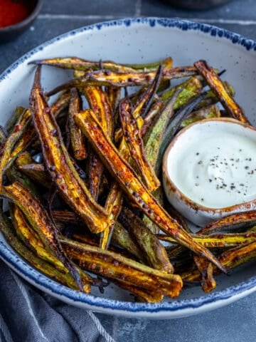 Crispy okra fries in a white bowl accompanied by a yogurt sauce in a small bowl.