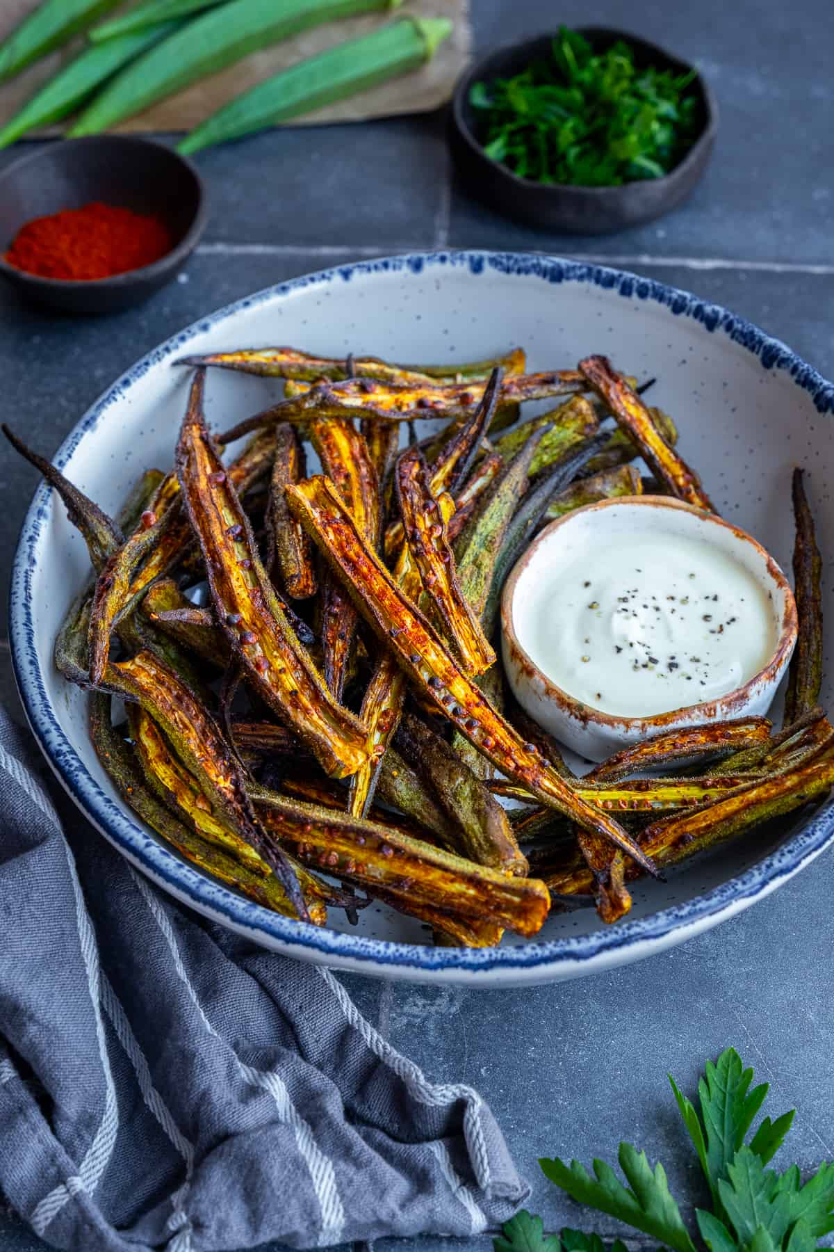 Okra fries in a white bowl accompanied by a yogurt sauce in a small bowl.