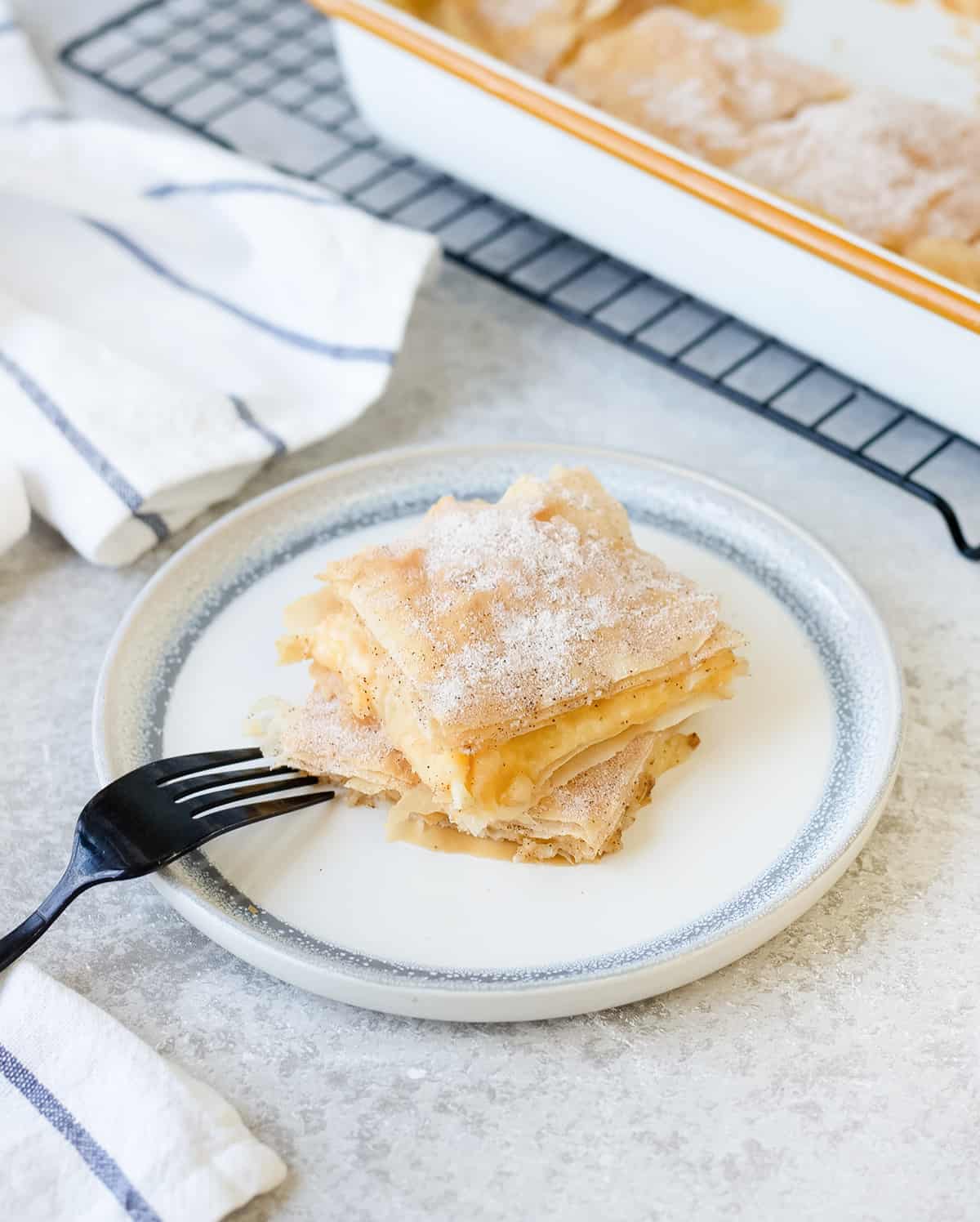 Filo custard pie slices garnished with powdered sugar on a white plate and a fork on the side.