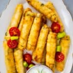 Cheese rolls with filo on an oval white plate and a yogurt sauce on the side.