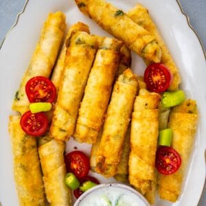 Cheese rolls with filo on an oval white plate and a yogurt sauce on the side.