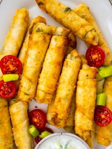 Cheese rolls with filo on an oval white plate and a yogurt sauce on the side.