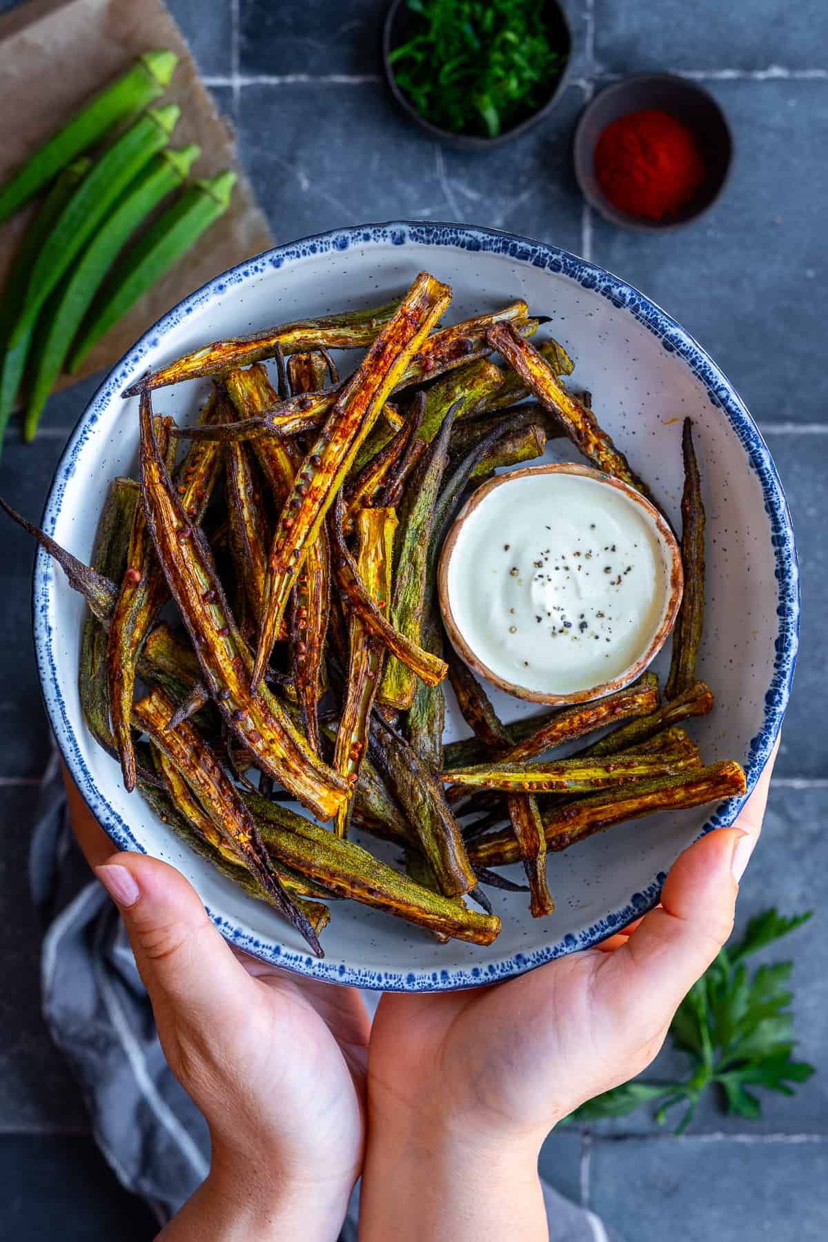 Hands holding a bowl of okra fries accompanied with a yogurt sauce.