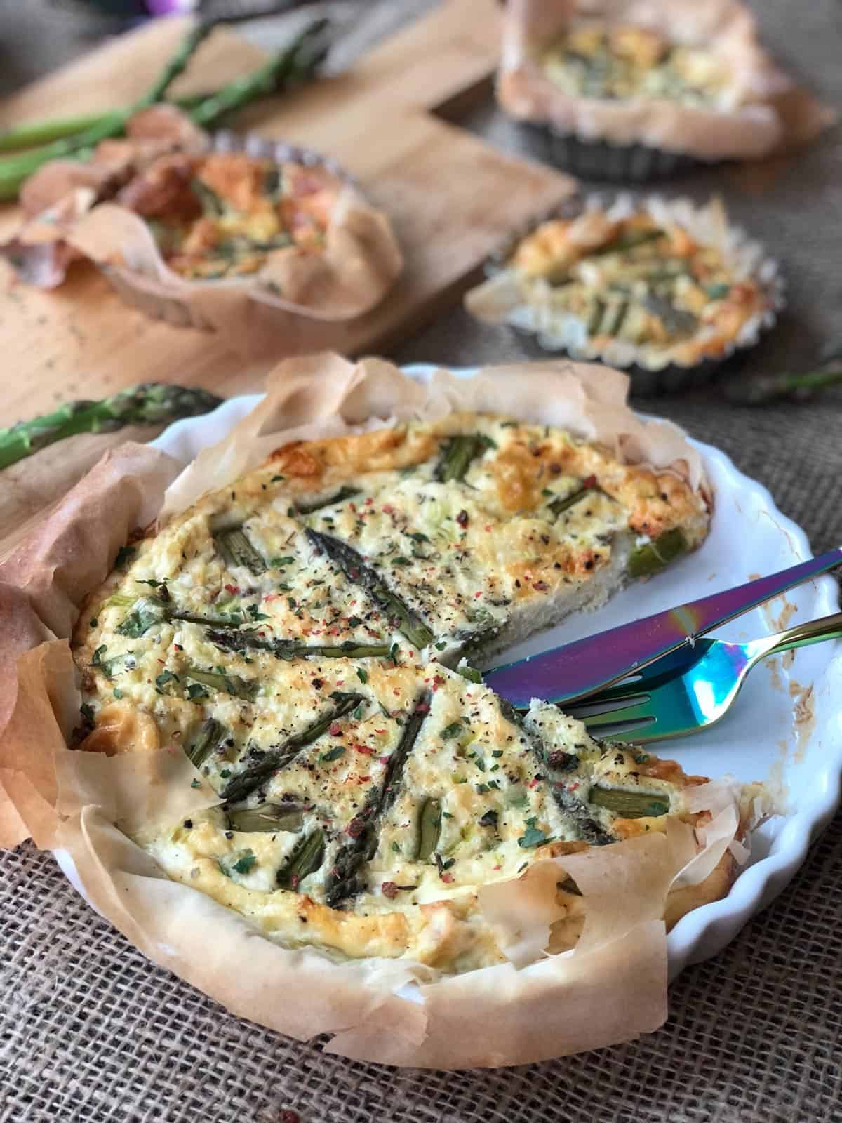 Filo quiche with asparagus on a plate, a slice taken, a fork and a knife on the side.