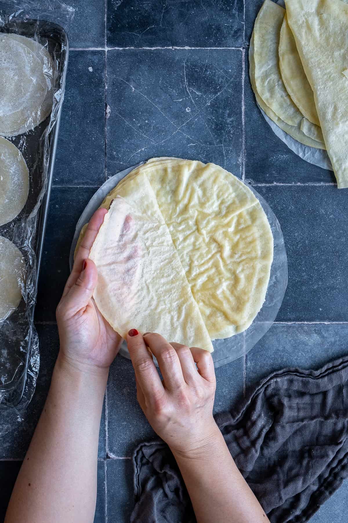 Hands separating a phyllo sheet from a stack on a grey marble background.