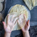 Hands holding super thin homemade phyllo sheets on a grey background.