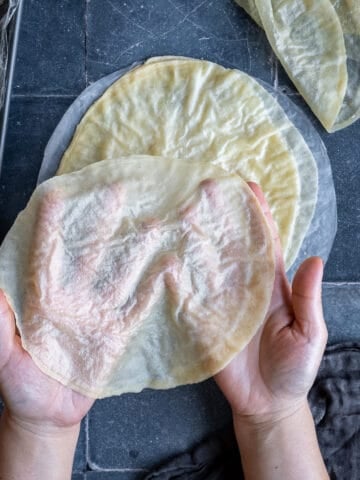 Hands holding super thin homemade phyllo sheets on a grey background.