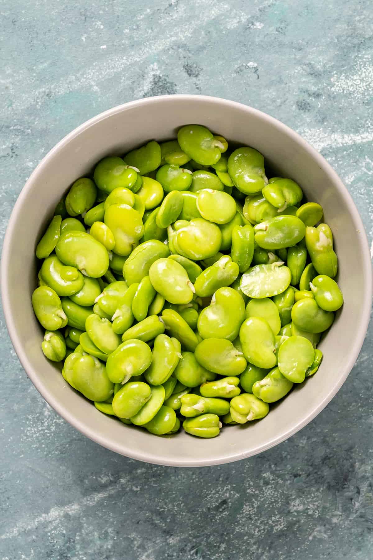 Shelled fresh fava beans in a white bowl.