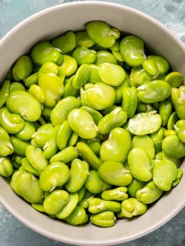 Shelled green fava beans in a white bowl.
