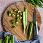 Fresh okra sliced in lengthwise and crosswise on a wooden cutting board and a knife on the side.