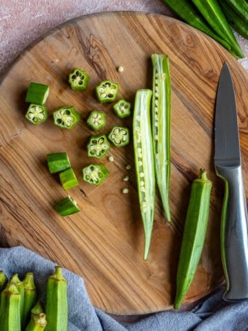 Fresh okra sliced in lengthwise and crosswise on a wooden cutting board and a knife on the side.