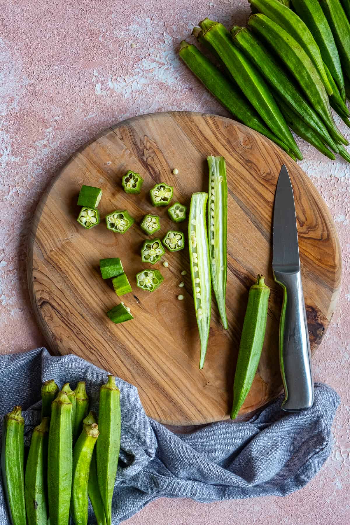 Fresh okra sliced in lengthwise and crosswise on a wooden cutting board and a knife on the side.