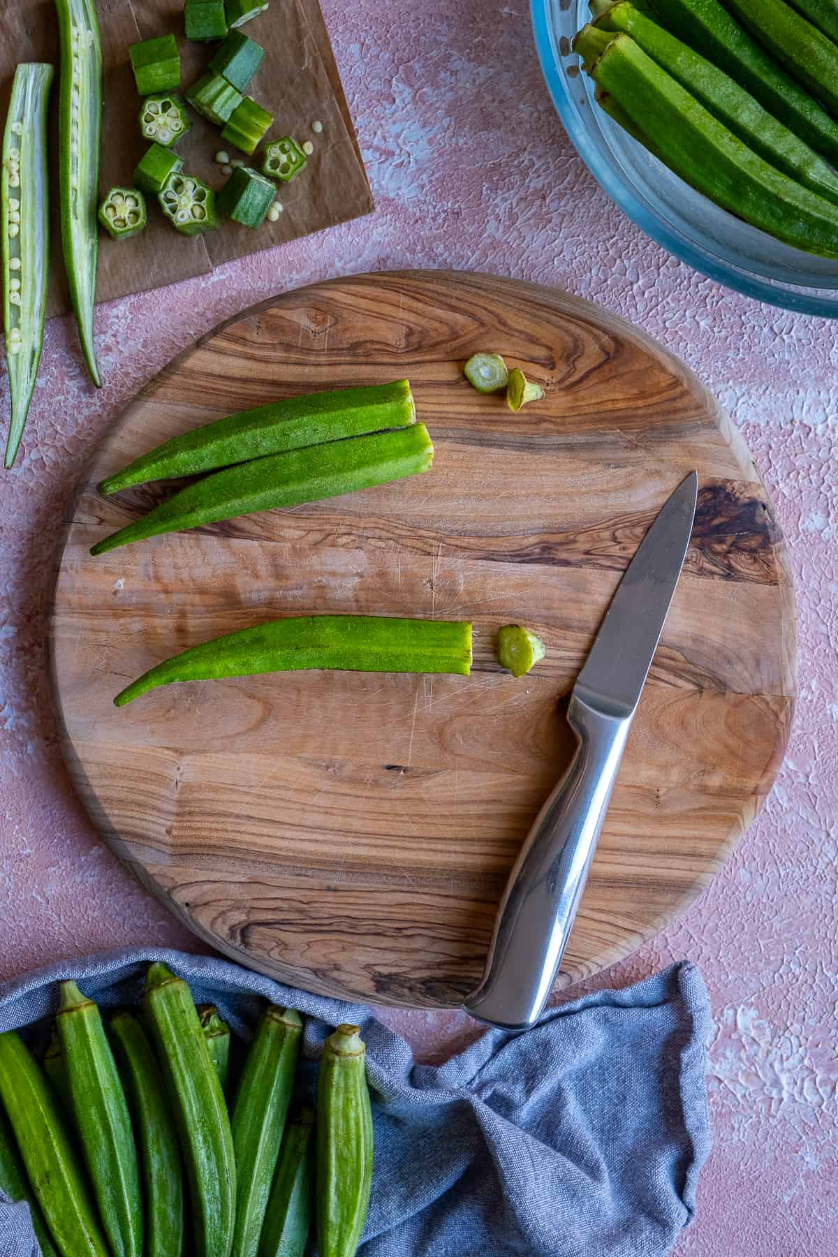 Okra pods being trimmed on a wooden board, a knife on the side.