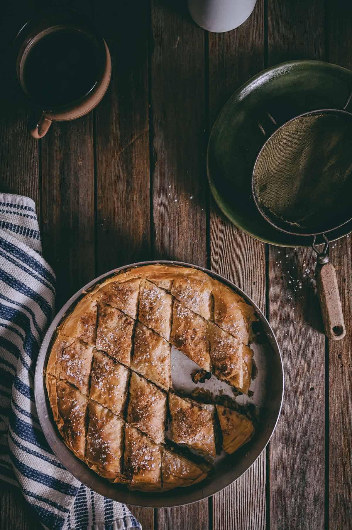 Greek pumpkin pie in a round baking pan on a wooden backdrop.