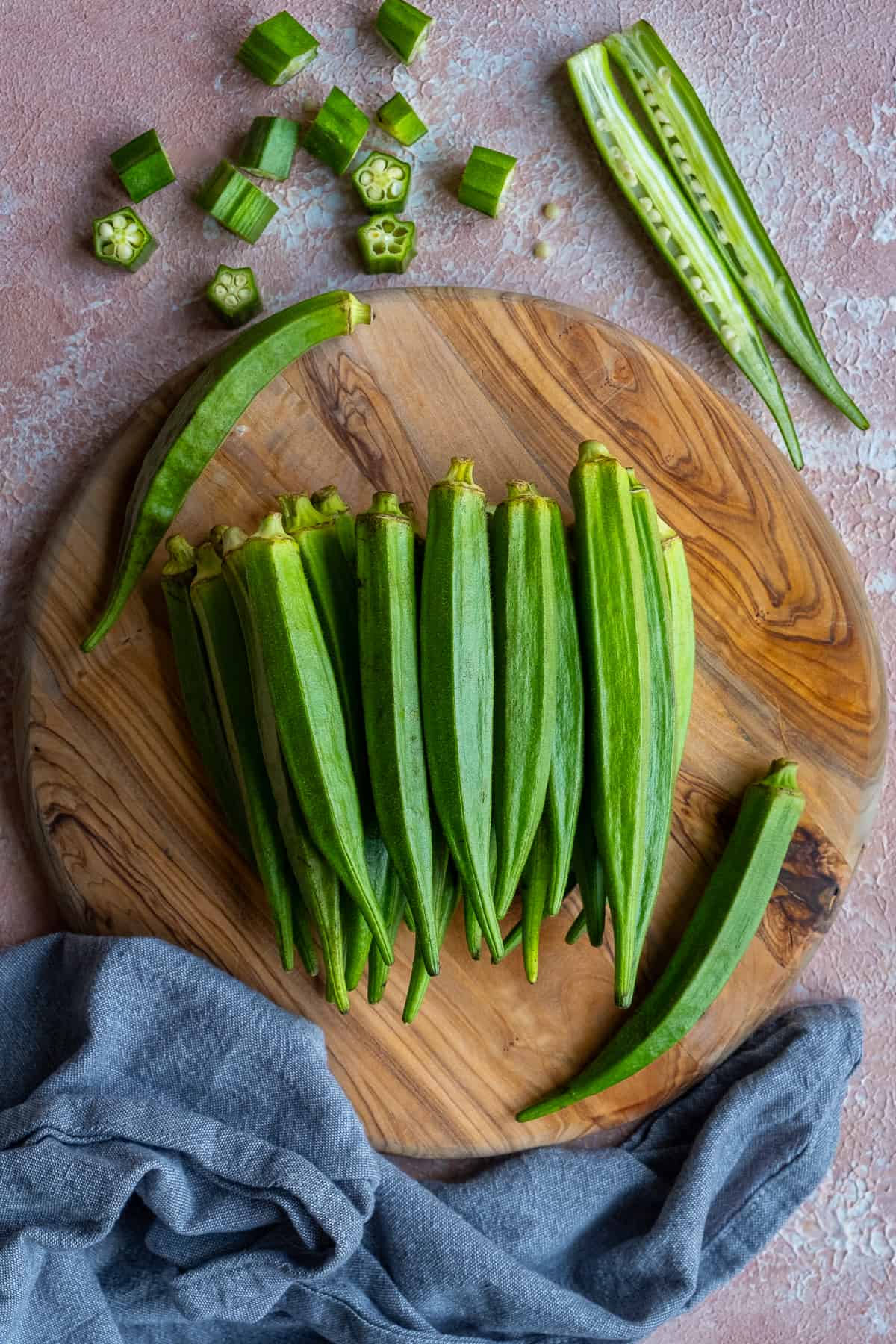 Fresh green okra pods on a round wooden cutting board.