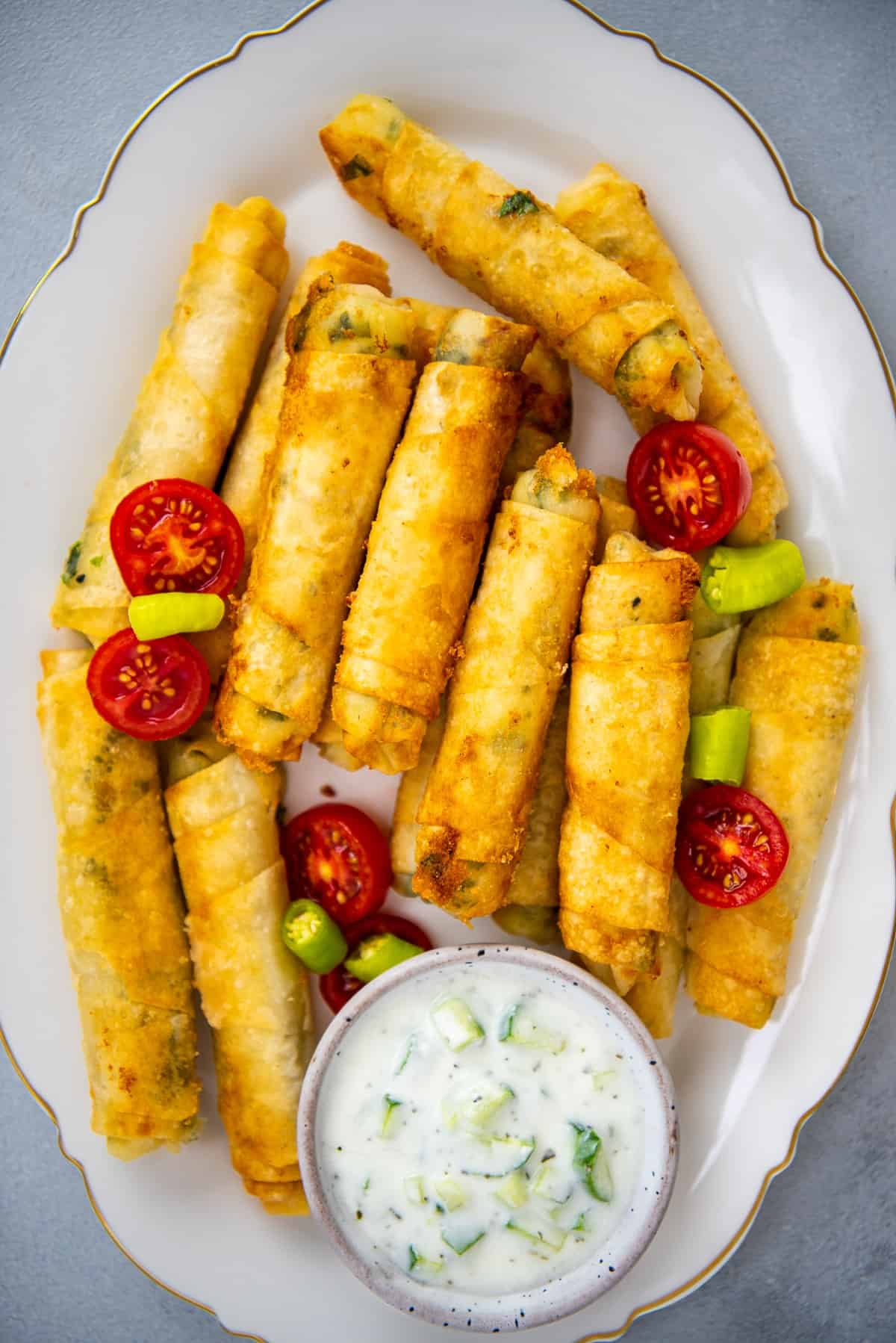 Phyllo dough rolls stuffed with cheese on an oval white plate and a yogurt sauce on the side.