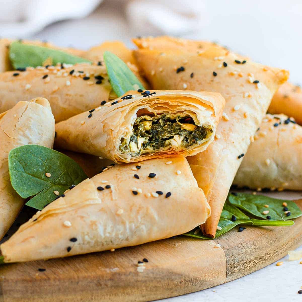 Spinach phyllo triangles stacked on a wooden cutting board.