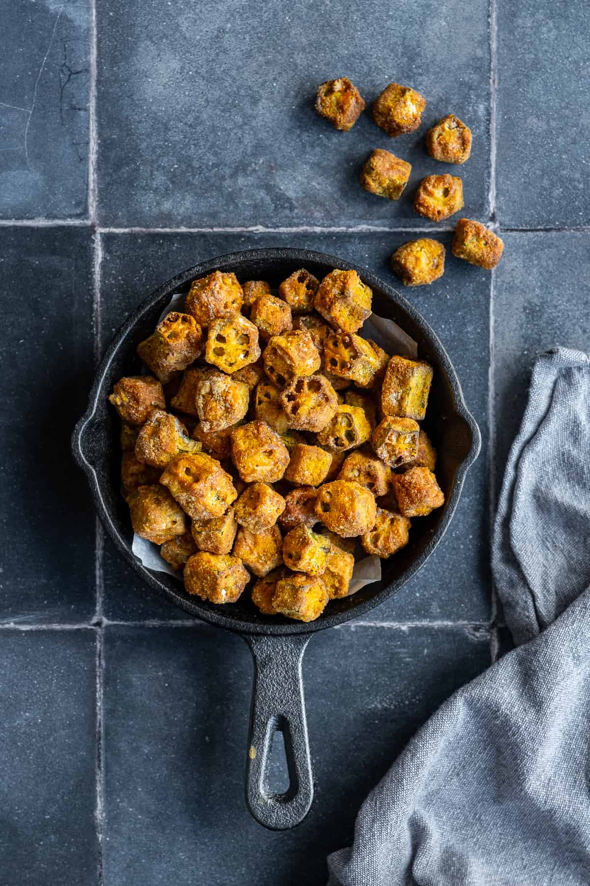 Fried okra loaded in a black pan on grey tiles.