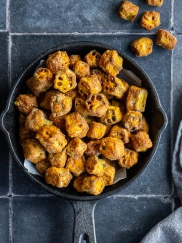 Breaded fried okra in a small cast iron pan photographed on a grey backdrop.