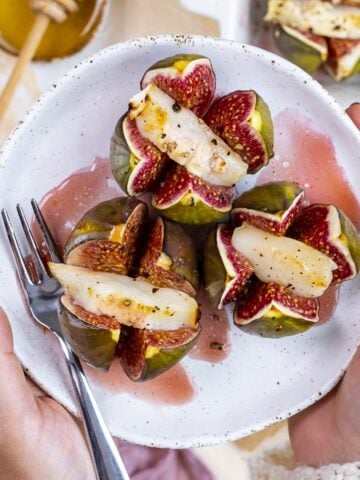 Hands holding a plate of goat cheese stuffed figs.