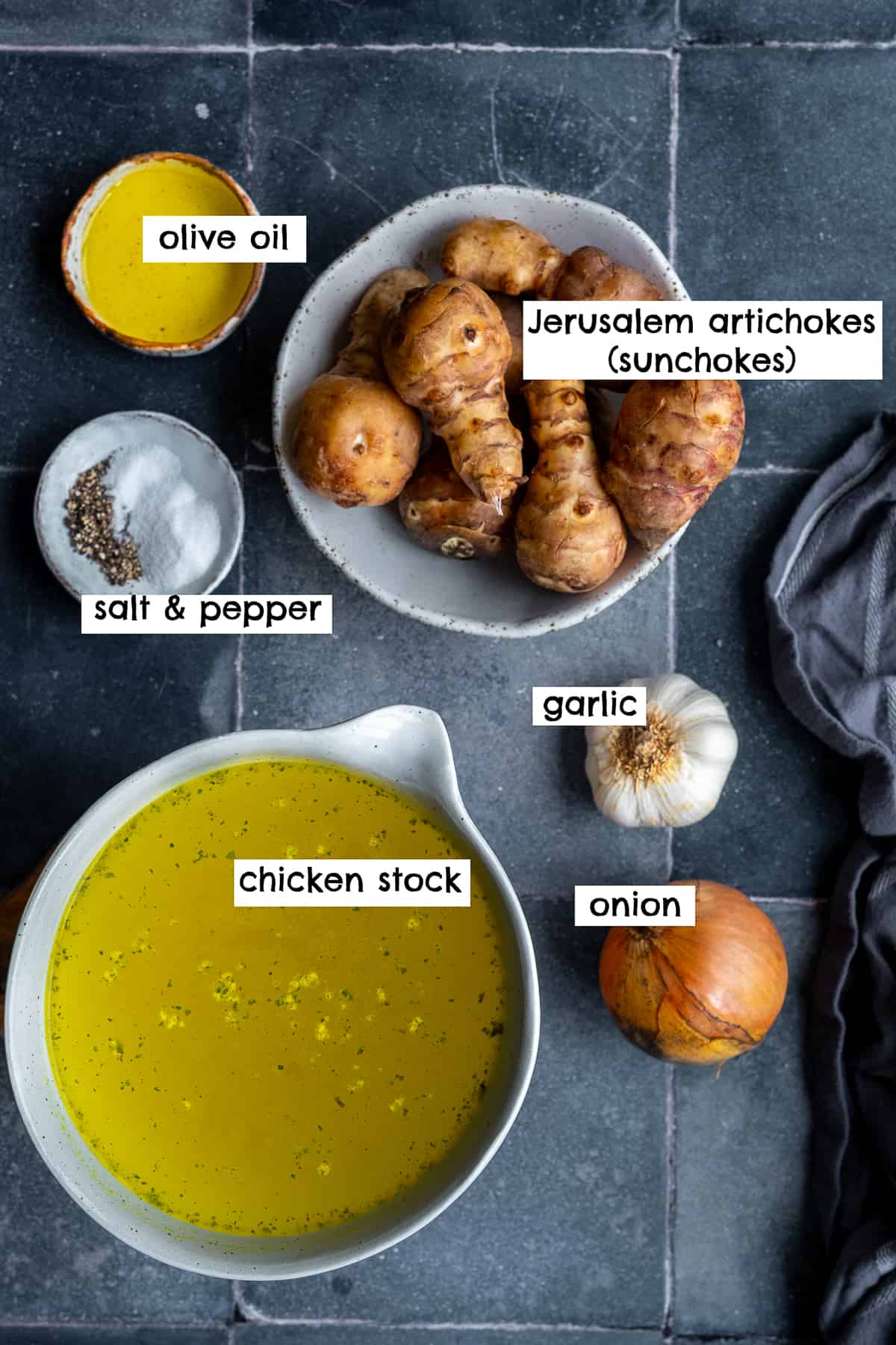 Jerusalem artichokes, onion, garlic, chicken stock, olive oil, salt and pepper on a dark background.