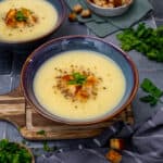 Jerusalem artichoke soup garnished with croutons, parsley and pepper in a bluish bowl.