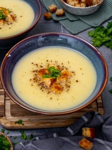 Jerusalem artichoke soup garnished with croutons, parsley and pepper in a bluish bowl.